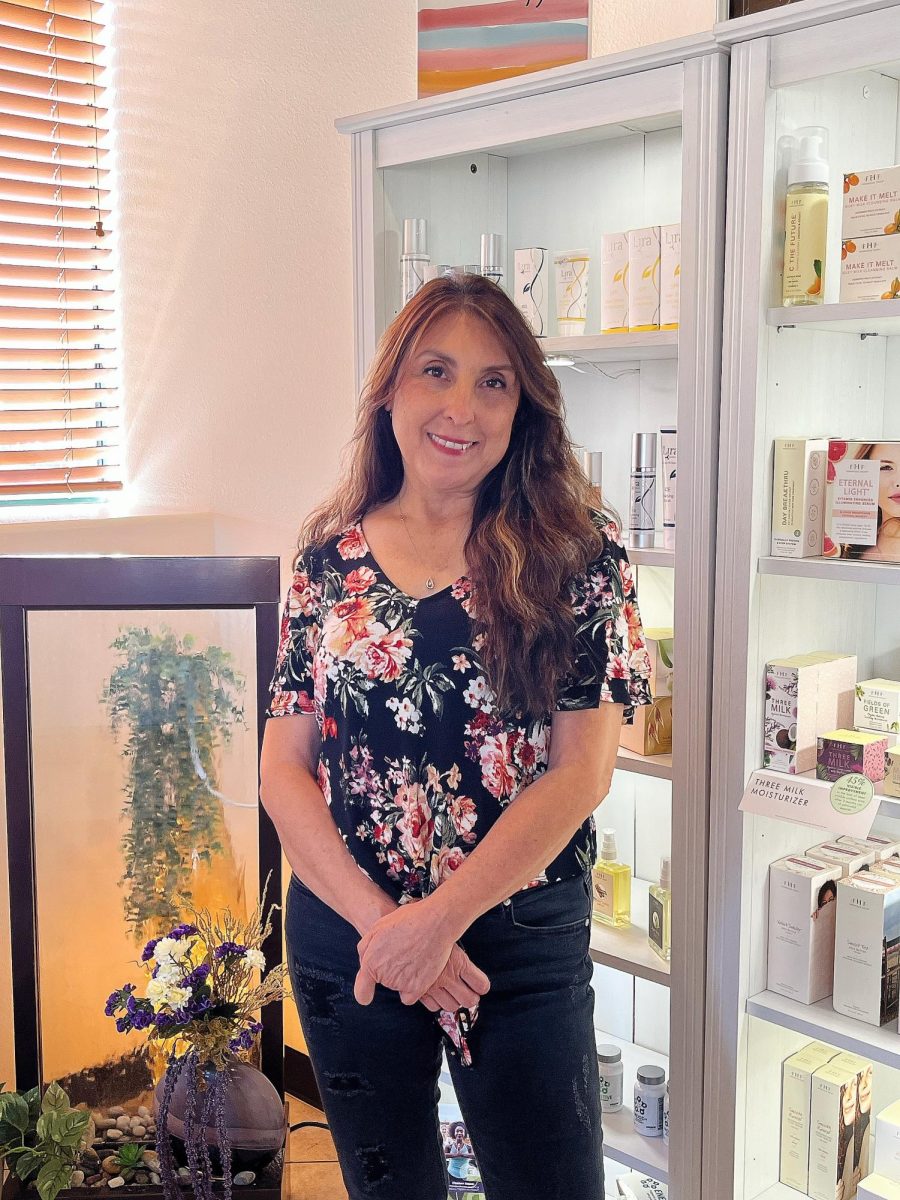 Urioste is at the front of Revitalize Skincare Studio, standing in front of a wall of her sourced products. Photo by Kooper Carroll.