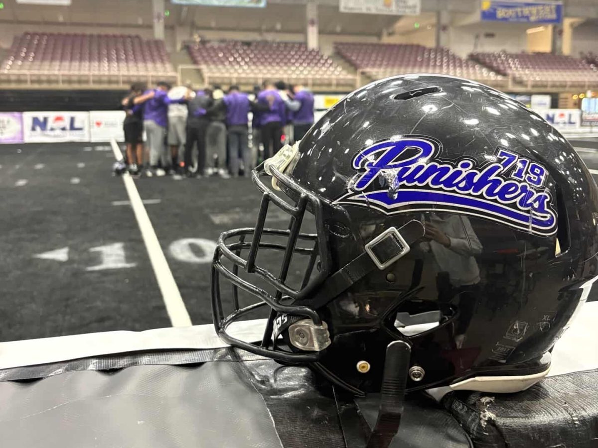The Punishers helmet, with the team in a prayer during pregame in the background.(photo by Donovan Trujillo).